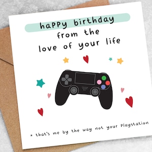 May include: A white card with a black and white illustration of a video game controller. The card has the text "happy birthday from the love of your life * that's me by the way not your Playstation" on it.