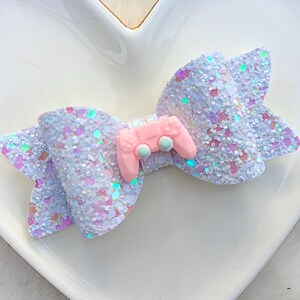 May include: A white glitter bow with a pink and blue video game controller charm.