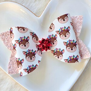 May include: A pink and white glitter bow with a reindeer pattern. The bow has a red bow in the center.