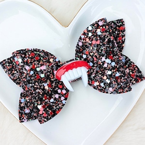 May include: A black and red glitter bow with a red and white vampire teeth embellishment.