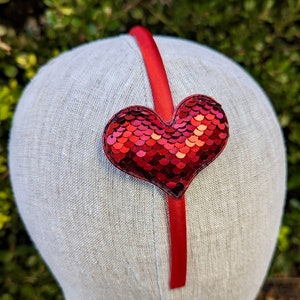 May include: Red headband with a red sequin heart. The headband is made of satin ribbon.