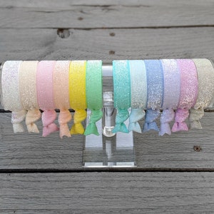 May include: A set of 10 colorful glitter hair scrunchies in a rainbow color scheme. The scrunchies are displayed on a clear acrylic stand.