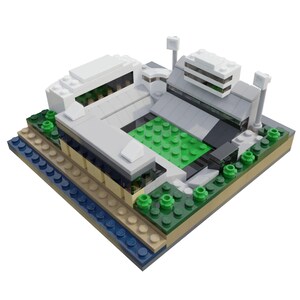 Puede incluir: Un modelo de estadio en miniatura construido con bloques de juguete. El modelo presenta un campo de juego verde, edificios grises y blancos, y peque&ntilde;os &aacute;rboles verdes. La base incluye capas de ladrillos azules, beige y marrones.