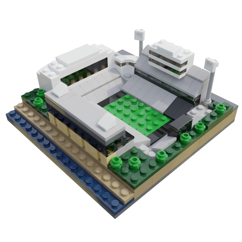 Puede incluir: Un modelo de estadio en miniatura construido con bloques de juguete. El modelo presenta un campo de juego verde, edificios grises y blancos, y peque&ntilde;os &aacute;rboles verdes. La base incluye capas de ladrillos azules, beige y marrones.
