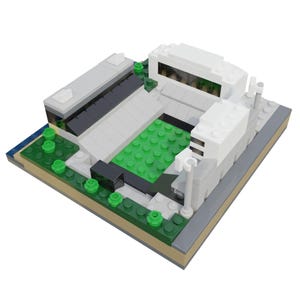 Puede incluir: Maqueta de estadio en miniatura construida con bloques de construcci&oacute;n coloridos. El modelo presenta un campo verde, gradas grises y estructuras blancas, con peque&ntilde;os &aacute;rboles verdes alrededor del per&iacute;metro. La base es beige y gris.