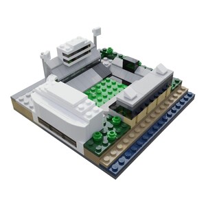 Puede incluir: Maqueta de estadio en miniatura construida con bloques de juguete. El modelo presenta un campo de juego verde, gradas blancas y grises, y varios detalles arquitect&oacute;nicos. Peque&ntilde;os &aacute;rboles verdes y detalles azules y beige a&ntilde;aden color.