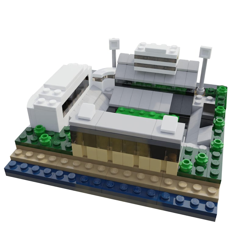 Puede incluir: Maqueta arquitect&oacute;nica en miniatura construida con bloques de construcci&oacute;n de juguete de colores. El modelo presenta un dise&ntilde;o de varios niveles con estructuras grises, blancas y beige, acentuadas con bloques verdes y azules. Se ven dos farolas.