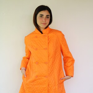 May include: A bright orange quilted coat with a double-breasted closure and a diamond pattern. The coat has a stand-up collar and long sleeves.