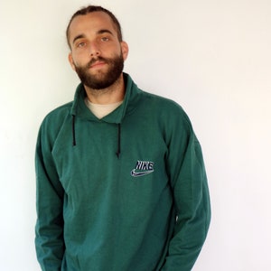Könnte beinhalten: Ein dunkelgrüner, langärmliger Pullover mit einem schwarzen Kordelzug und einem weißen Nike-Logo mit dem Wort "NIKE" in Schwarz.