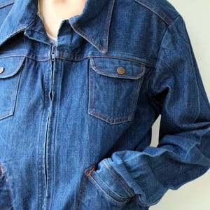 May include: A blue denim jacket with a zipper closure, two chest pockets, and two front pockets. The jacket has a collar and long sleeves.
