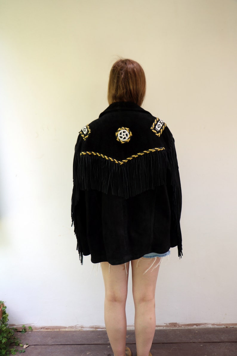 May include: Black suede jacket with gold and white embroidery and fringe detailing. The jacket has a western style.