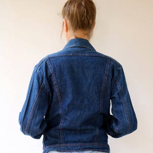 May include: A dark blue denim jacket with red stitching. The jacket has a classic style with a button-up front and long sleeves.