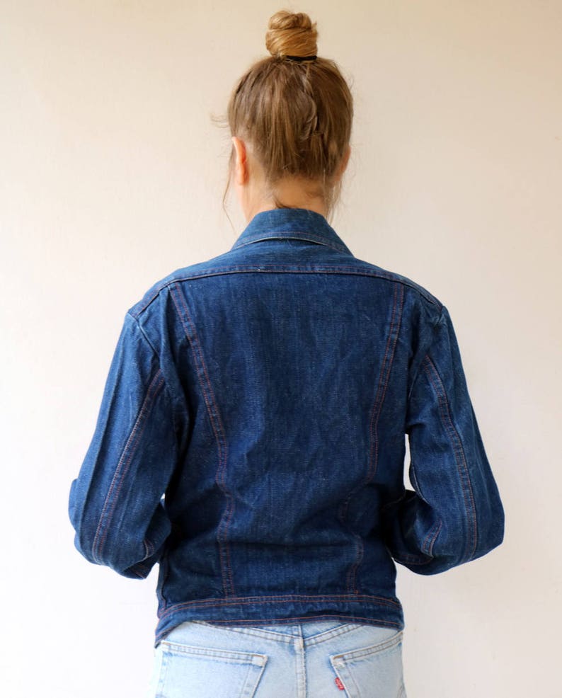 May include: A dark blue denim jacket with red stitching. The jacket has a classic style with a button-up front and long sleeves.