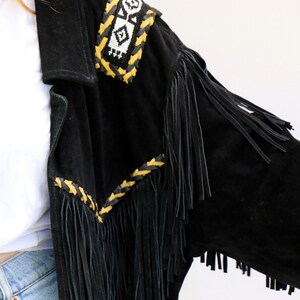 May include: Black suede jacket with fringe detailing and a beaded and braided trim in yellow and white.