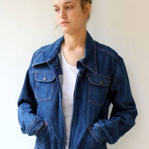 May include: A blue denim jacket with a zipper closure and two flap pockets. The jacket has a collar and long sleeves.