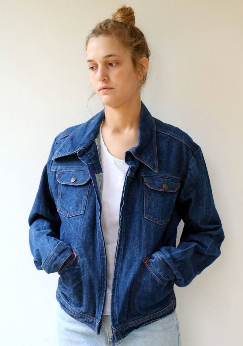 May include: A blue denim jacket with a zipper closure and two flap pockets. The jacket has a collar and long sleeves.