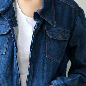 May include: A dark blue denim jacket with a zipper closure and a single chest pocket. The jacket has a classic style and is made of a durable material.
