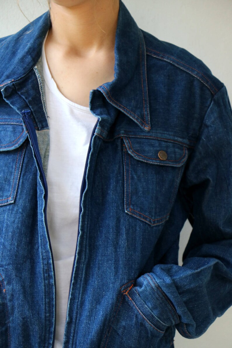 May include: A dark blue denim jacket with a zipper closure and a single chest pocket. The jacket has a classic style and is made of a durable material.