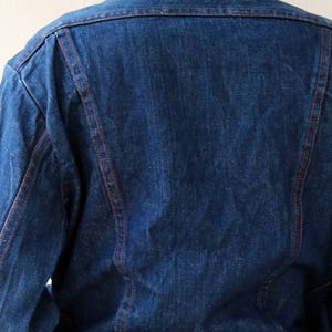 May include: A blue denim jacket with red stitching. The jacket has a classic style and is made of a durable material.