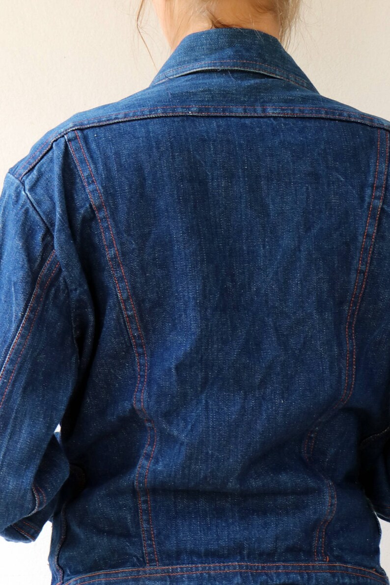 May include: A blue denim jacket with red stitching. The jacket has a classic style and is made of a durable material.