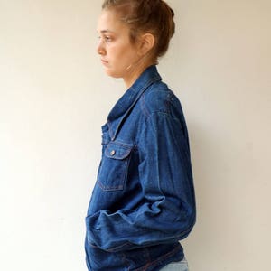 May include: A blue denim jacket with a collared neckline and long sleeves. The jacket has a button closure and two front pockets.