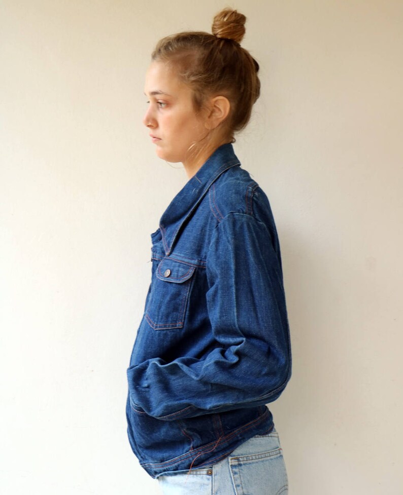 May include: A blue denim jacket with a collared neckline and long sleeves. The jacket has a button closure and two front pockets.