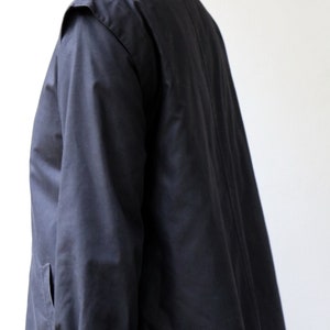 May include: A long-sleeved black jacket with a high collar and a single button fastening. The jacket has a long, flowing design and features a buckle detail on the sleeve.