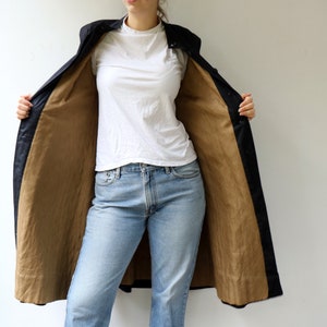 May include: A long black coat with a brown lining. The coat is open and the person wearing it is showing off the lining. The person is wearing blue jeans and a white t-shirt.