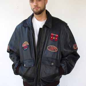 May include: Black leather Levi Strauss & Co. bomber jacket with multiple patches. Features a zip-up front, two front pockets, and brown ribbed cuffs. Patches include the Levi's logo and a red, white, and blue shield.