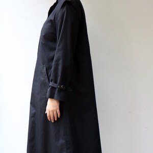 May include: A long black coat with a stand-up collar and a buckle detail on the sleeves.