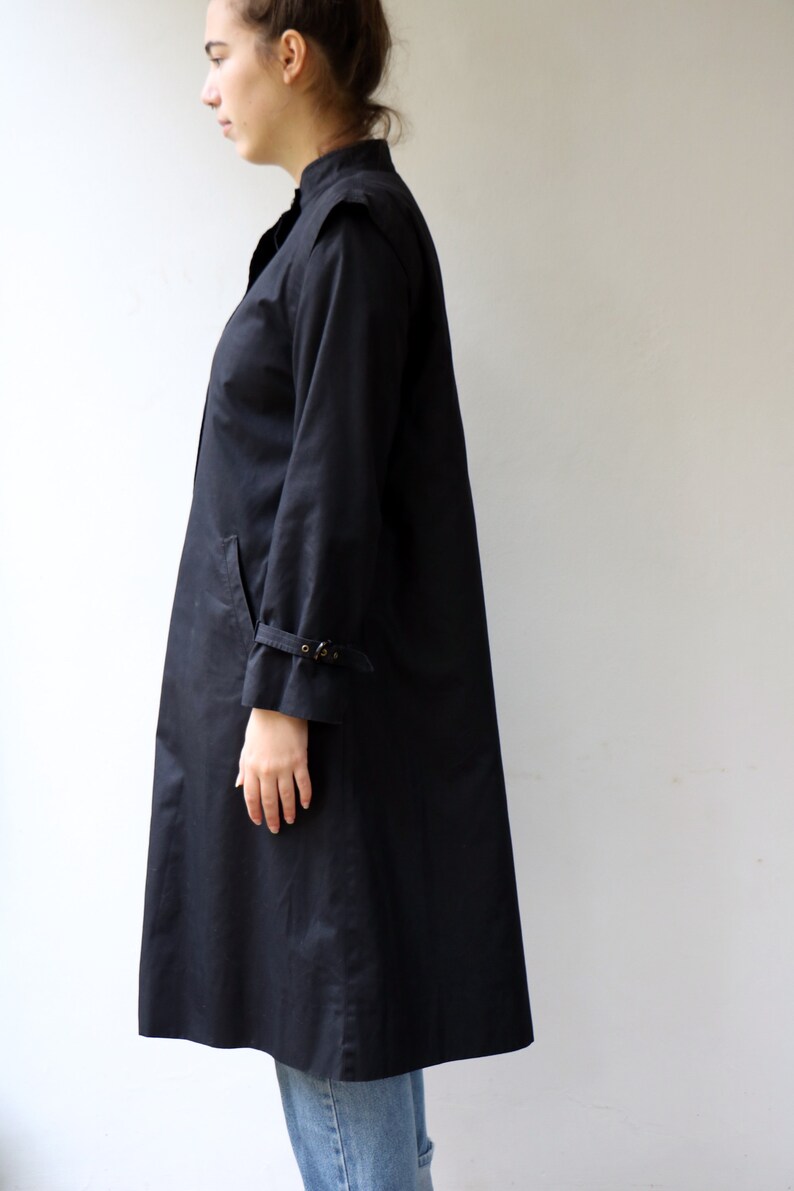 May include: A long black coat with a stand-up collar and a buckle detail on the sleeves.