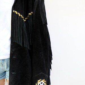 May include: A black suede jacket with fringe detailing and yellow and white embroidered accents. The jacket has a button closure and a collar.