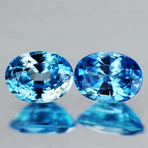 May include: Two oval-shaped, faceted gemstones with a light blue to dark blue color gradient. The gemstones are set against a white background.