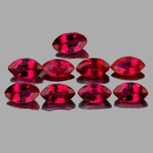 May include: Nine marquise-cut gemstones with a deep red hue are arranged on a reflective surface. The gems have facets that catch the light, creating a sparkling effect. The arrangement suggests a collection of precious stones.