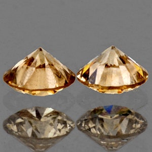 May include: Two round, faceted, brown diamonds. The diamonds are set in a classic round shape and have a brilliant cut.