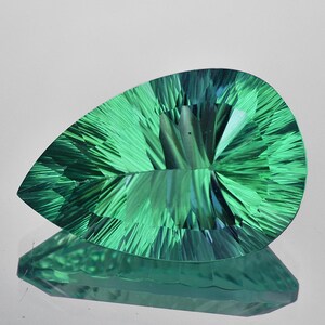 May include: A pear-shaped green gemstone with a faceted cut. The gemstone has a striated pattern and a light blue hue.
