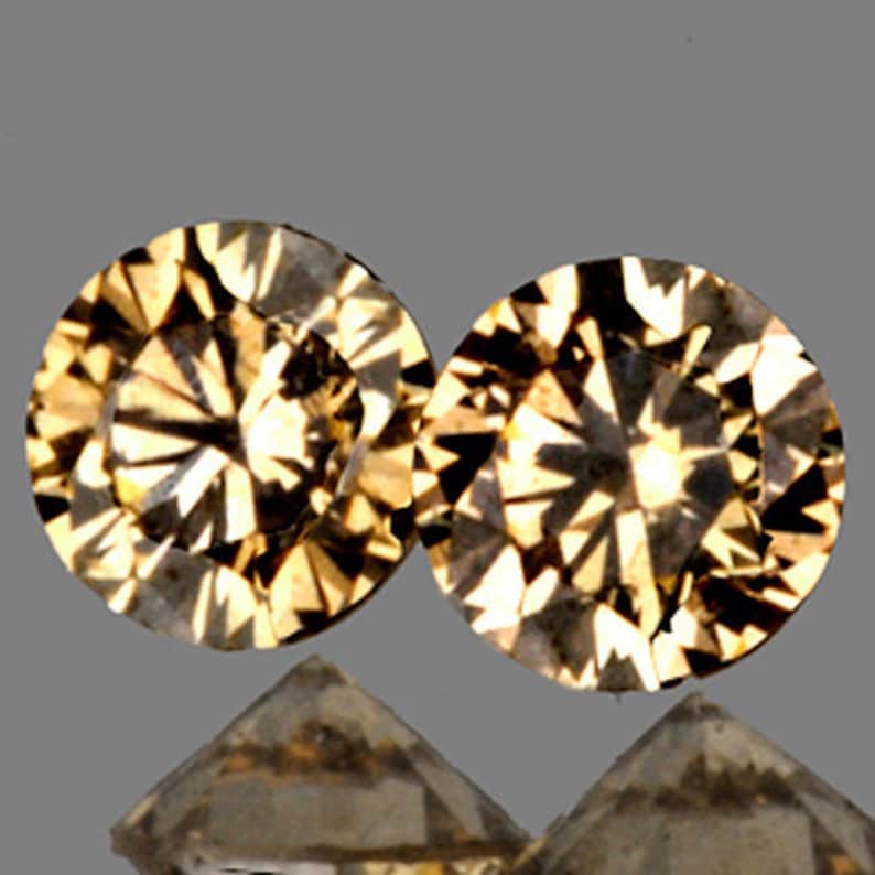 May include: Two round, faceted, brown gemstones with a starburst pattern. The gemstones are set against a gray background.