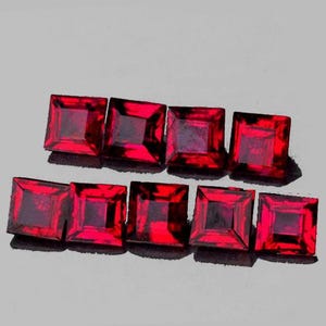 May include: Nine square-cut, deep red gemstones arranged in two rows. Each stone features a faceted surface that reflects light, creating a vibrant crimson appearance. The gems are uniform in shape and color, displaying a clear, transparent quality.