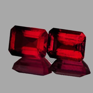 May include: Two deep red emerald cut gemstones.