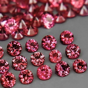 Könnte beinhalten: Eine Sammlung runder, facettierter, rosafarbener Edelsteine. Die Edelsteine sind in einem verstreuten Muster auf einer weißen Oberfläche angeordnet.