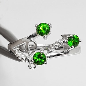 May include: A silver ring with three green gemstones set in a delicate, twisted design.