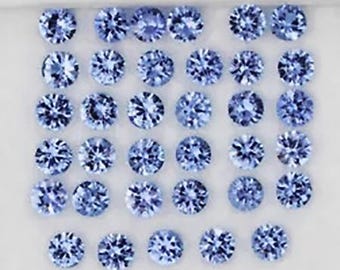 May include: A collection of thirty-four round, faceted light blue gemstones arranged in a grid pattern. Each stone features a brilliant cut with multiple facets that reflect light, creating a sparkling appearance against a plain white background.