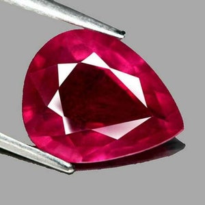 May include: A deep red pear-shaped gemstone with a faceted cut. The gemstone is held by a pair of tweezers.