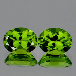 May include: Two oval-shaped green peridot gemstones. The gemstones are faceted and have a bright, vibrant green color.