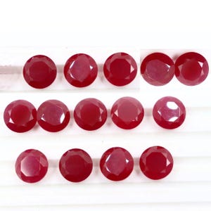Puede incluir: Una colección de gemas redondas, facetadas, de color rojo intenso. Las gemas están dispuestas en filas, cada una mostrando un brillo brillante. El color es consistente en todas partes, con una superficie pulida que refleja la luz. Estas gemas son probablemente rubíes.