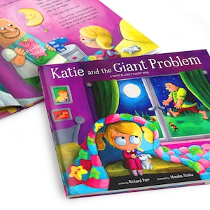 May include: A purple book titled "Katie and the Giant Problem: A Magic Blanket Tales Book" with a colorful illustration of a girl under a blanket with stars on it. The book is open to a page with a night scene and a giant figure in the window.