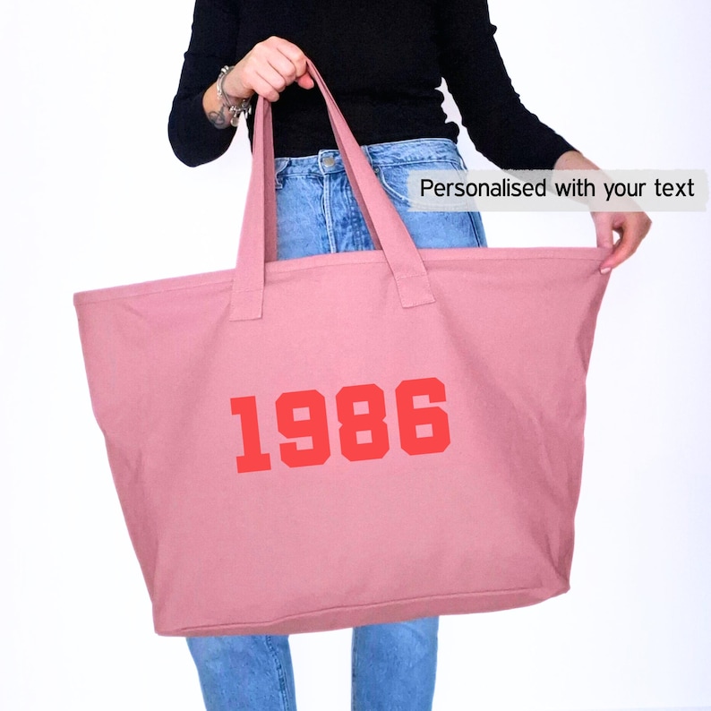 May include: A large pink tote bag with the year "1986" printed in red block letters. The bag has long handles and the text "Personalised with your text" is visible.