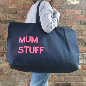 Könnte beinhalten: Eine große schwarze Tragetasche mit pinkfarbenem Schriftzug "MUM STUFF".