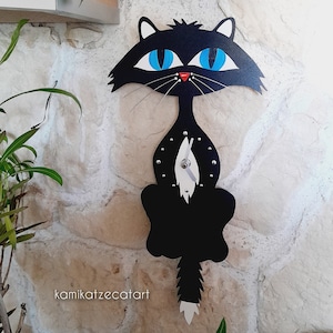 May include: Black cat wall clock with blue eyes and a white tail. The clock has a silver hand and a black background with white dots.