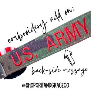 May include: A camouflage-patterned strap with the words "U.S. ARMY" embroidered in red. The text "embroidery add on" and "back-side message" are also present. The strap is likely a keychain or accessory.